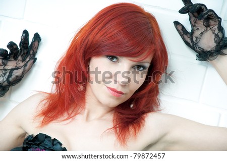 Sensual redheaded young woman standing by a white brick wall