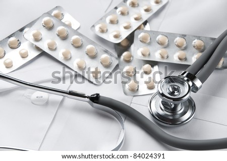 Blister packs full of tablets and stethoscope lying on doctor\'s smock