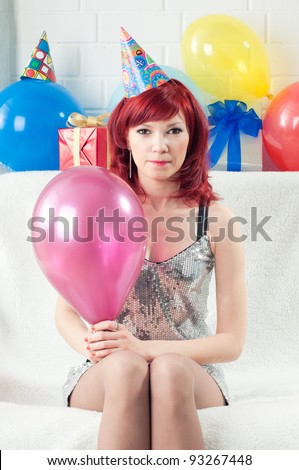 Red-haired party girl sitting on a sofa with a balloon and making a face