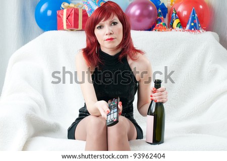 Annoyed red-haired party woman holding a wine bottle and watching TV