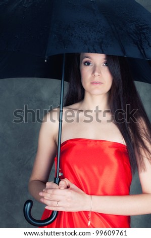 Studio portrait of a mysterious young woman in red sateen holding umbrella