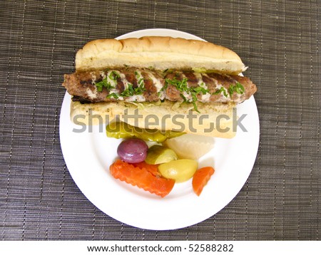 Kebab sandwich with pickles on white plate and brown fabric