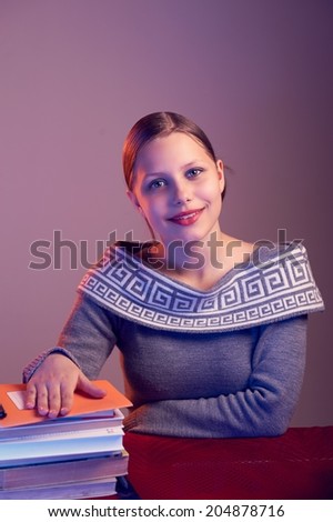 Cute happy teen girl sitting at table with books and smiling