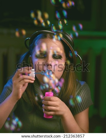 Sad teen girl sits and blows soap bubbles. Imprisoned in a dark room