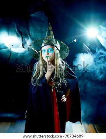 attractive little witch girl in mystical fog on dark background