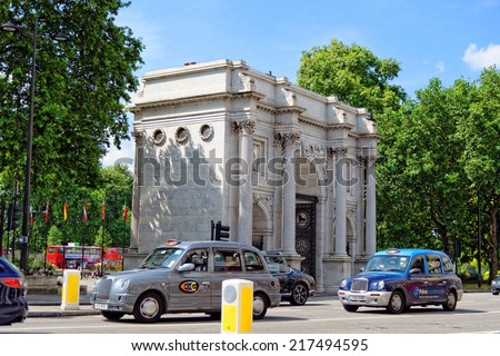 LONDON - JULY 1, 2014. Typical London cabs are passing by the Marble arch -  a 19th-century white marble triumphal arch and London landmark. Marble Arch was designed by John Nash in 1827.
