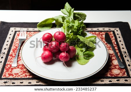 Raw fresh radishes on a white plate with a fork and a knife