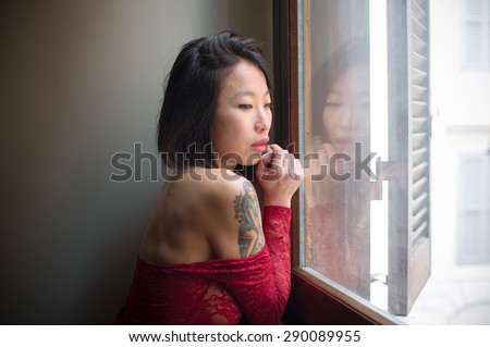 Beautiful seductive young asian woman posing thoughtful, red sexy body suite, window daylight