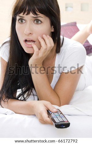 Attractive young woman watching a scary movie in tv alone in a room