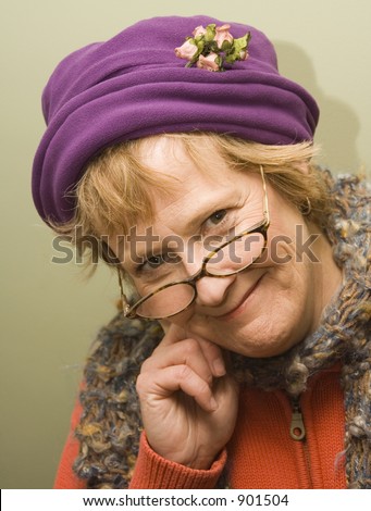 Beautiful older woman with a fun expression wearing a purple hat and red sweater.