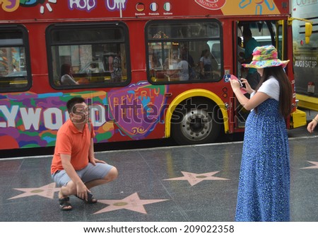 HOLLYWOOD, CA - AUGUST 3, 2014: A man crouches next to a celebrity star on the Hollywood, California Walk of Fame on August 3, 2014 as a woman stands nearby taking his photo.