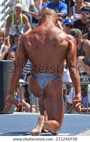 VENICE, CA SEPTEMBER 1, 2014: His back to the camera, a bodybuilder poses dramatically on one knee during the Muscle Beach Championship on September 1, 2014 at Venice Beach, CA.