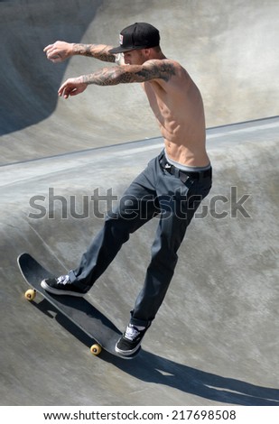 VENICE, CA - SEPTEMBER 1, 2014: Profile of a shirtless boy with a black baseball cap skateboarding up an small but steep incline at the Venice Skate Park in Venice, California on September 1, 2014.