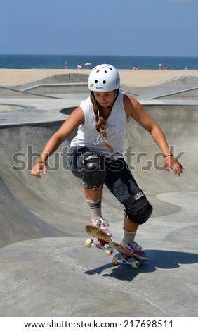 VENICE, CA - SEPTEMBER 1, 2014: A young girl wearing a helmet and knee pads raises the front end of her skateboard as she rides at the Venice Skate Park in Venice, California on September 1, 2014.