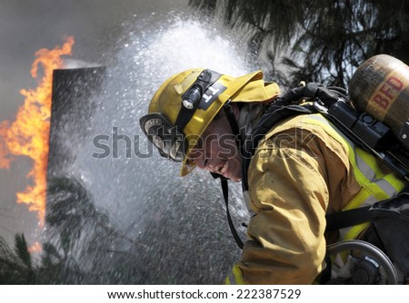 BURBANK, CA - MAY 27, 2013: A fireman sprays water on a burning building as he turns his head back toward the camera while battling a fire in Burbank, California on May 27, 2013.