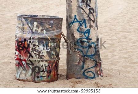 Graffiti covered trash can chained to a tree