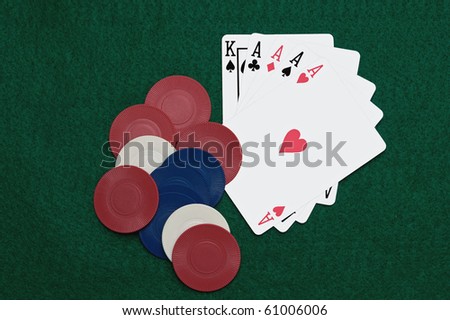 Poker Hand -- Five playing cards, a King and four Aces, fanned out and tucked beneath a small pile of gaming chips on a green felt background