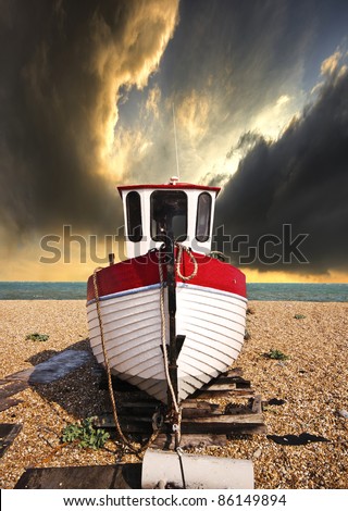 a beached fishing boat waiting for the tide on a shingle beach with the sea and a dramatic sky in the background