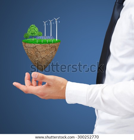 Businessman hand holding wind power station mills and trees on the lawn. Natural concept.