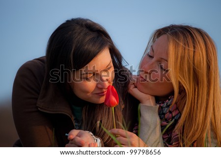 two friends smell a flower