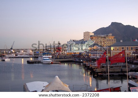 Beautifull day at Cape Town wharf. Some restaurants and bar on the left. Vessels are docked in the background.