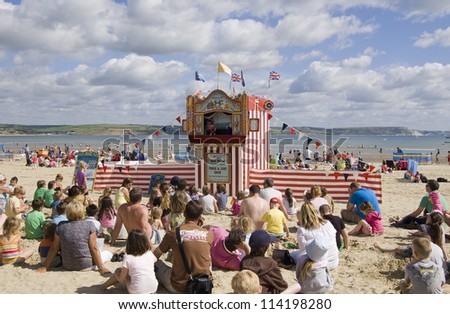 WEYMOUTH, DORSET, ENGLAND - AUGUST 31: Holiday makers sitting on the sands of Weymouth beach to watch a Punch and Judy show on August 31 2012.  The performance is attracting more tourists to the area.