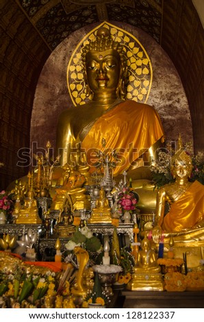 Historic golden Buddha surrounded by religious offerings at the temple of Wat Chet Yot, Chiang Mai, Thailand.