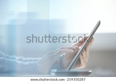 Human hands using tablet computer at office behind the glass door