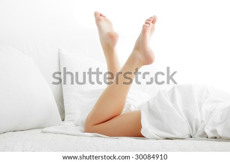 Woman legs on the bed with white bed clothes