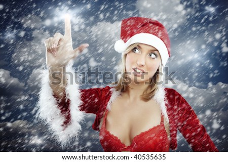 Sexy lady in revealed Santa costume with red brassiere touching stars on the sky during Christmas snowstorm