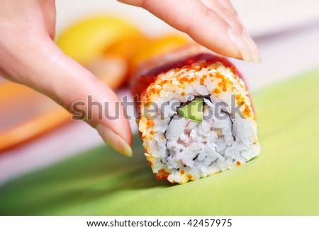 Close-up horizontal photo of the human hand taking rolled sushi with cucumber rice tuna and caviar. Shallow depth of field