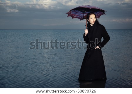 Single woman in the black coat standing in the water and holding umbrella. Creative symbol of the bad weather