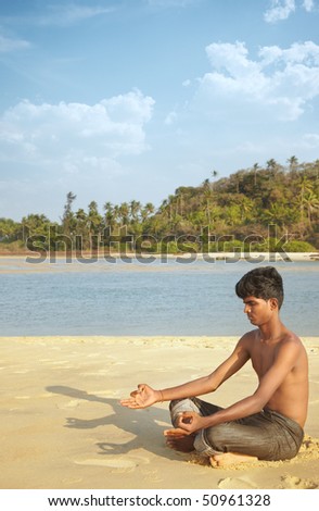 Indian man in cross-legged position at the summer beach doing Yoga meditation
