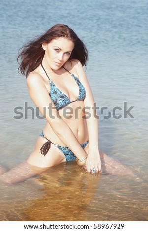 Elegant lady with perfect body in bikini sitting in the water under the sunlight