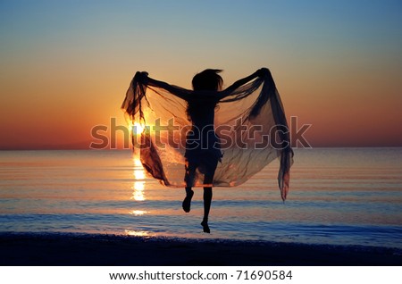 Rear view on the silhouette of the woman jumping at the beach during sunset. Natural darkness and colors