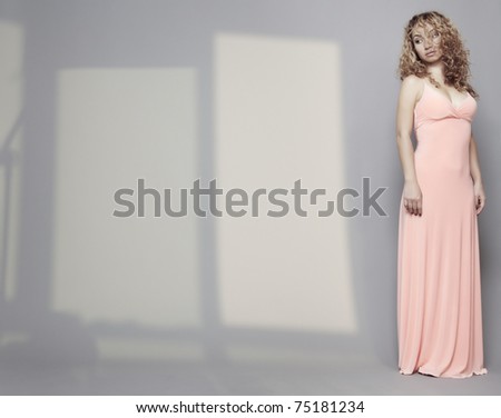Woman in pink dress with curly hairs standing alone in the interior with shadows