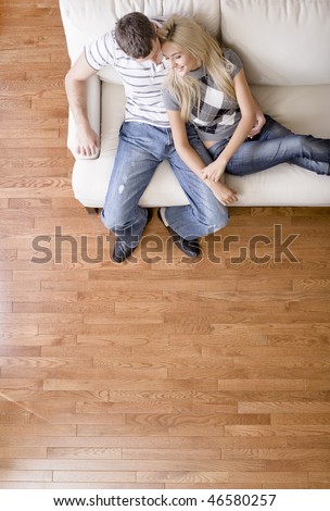 Cropped overhead view of affectionate couple sitting together on white love seat. Vertical format.