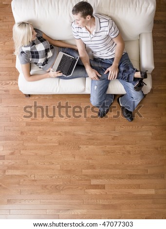 Full length overhead view of couple relaxing together on white couch, with woman using laptop and stretching out with her legs in the man\'s lap. Vertical format.