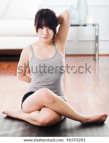 Asian woman sitting on a yoga mat doing the cow face pose.