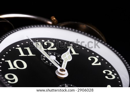 Old alarm clock on black background with black clock face and white needles - landscape format