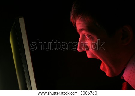 A man in shirt and tie screams at a red computer monitor. Anger? Frustration? Fear?
