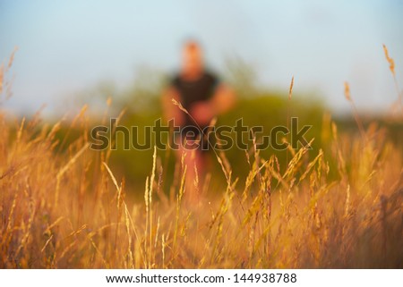 Young man is running on summer meadow - selective focus on grass