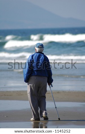 Am elderly person strolls down the beach alone.