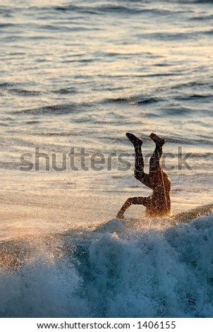 A silhouette of a surfer landing head first into the water.