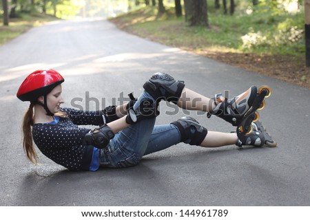 Girl fell down from roller skates, lying on the ground