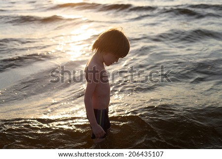Profile of sad boy with bowed head on background of the sea waves at sunset
