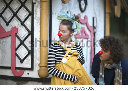 Clowns playing spies, woman and man with red noses and colorful clothing looking out of the corner