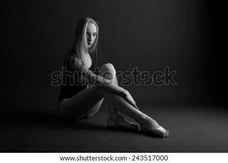 Young ballerina sitting on the studio floor bending the knees, monochrome