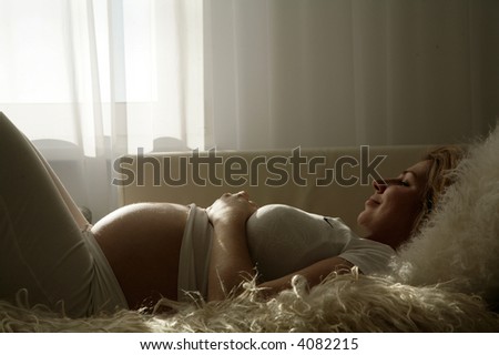 happy pregnant woman laying on bed holding hands on belly