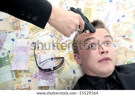 Man laying in money with gun pointed at head